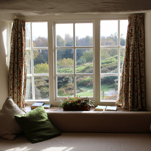 A scenic view of a large cosy window with pillows, cushions and books on the window sill.