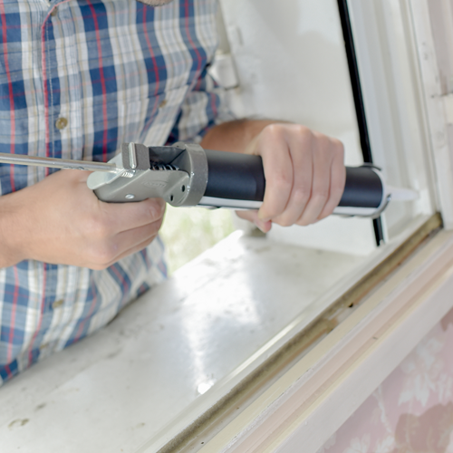 An image of a man applying glue or sealant to repair a window.