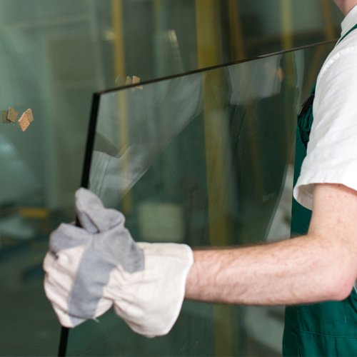 A picture of a man wearing gloves lifting a pane of glass.